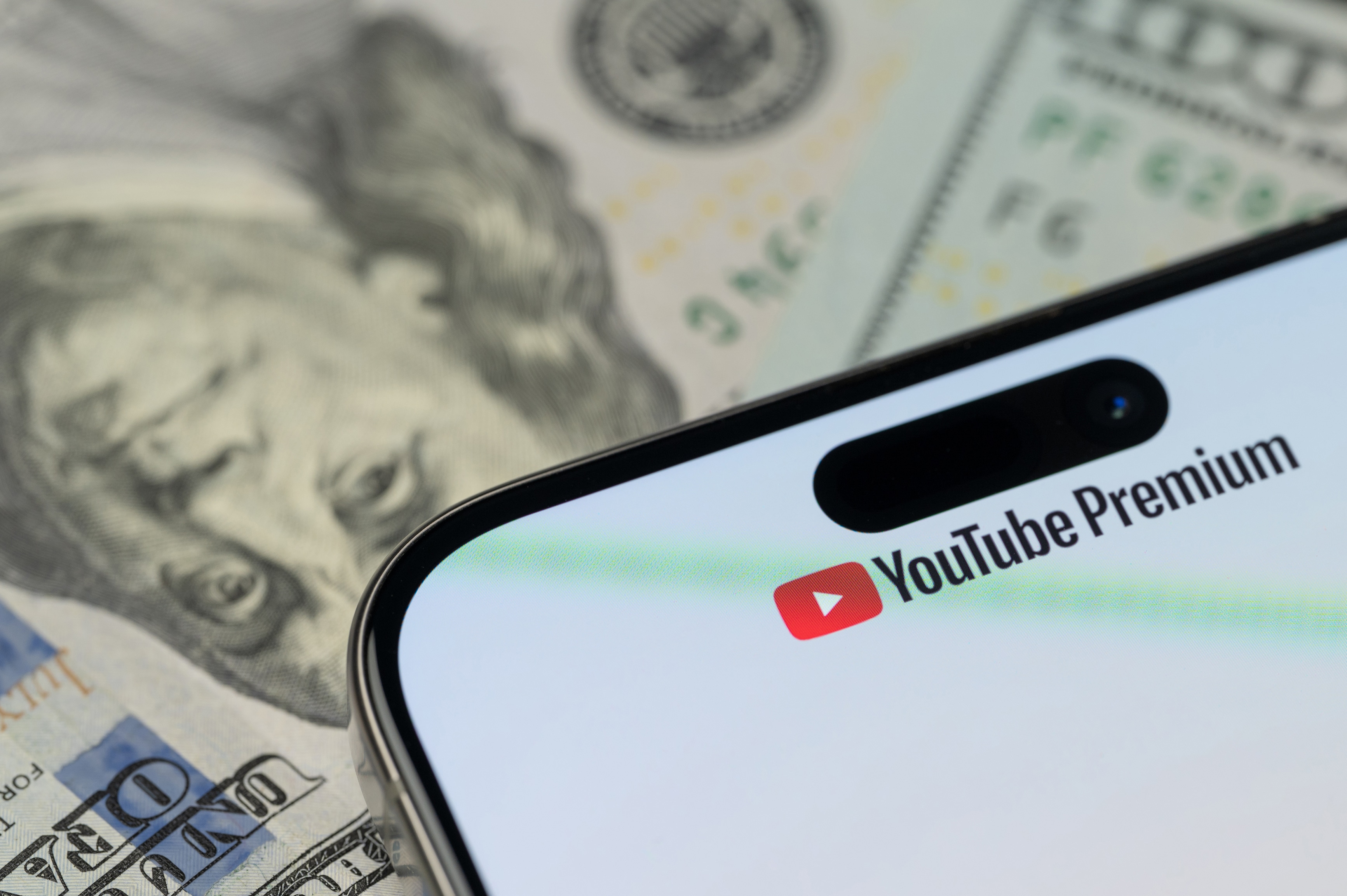 Logotipo de YouTube Premium en un iPhone sobre billetes de un dólar