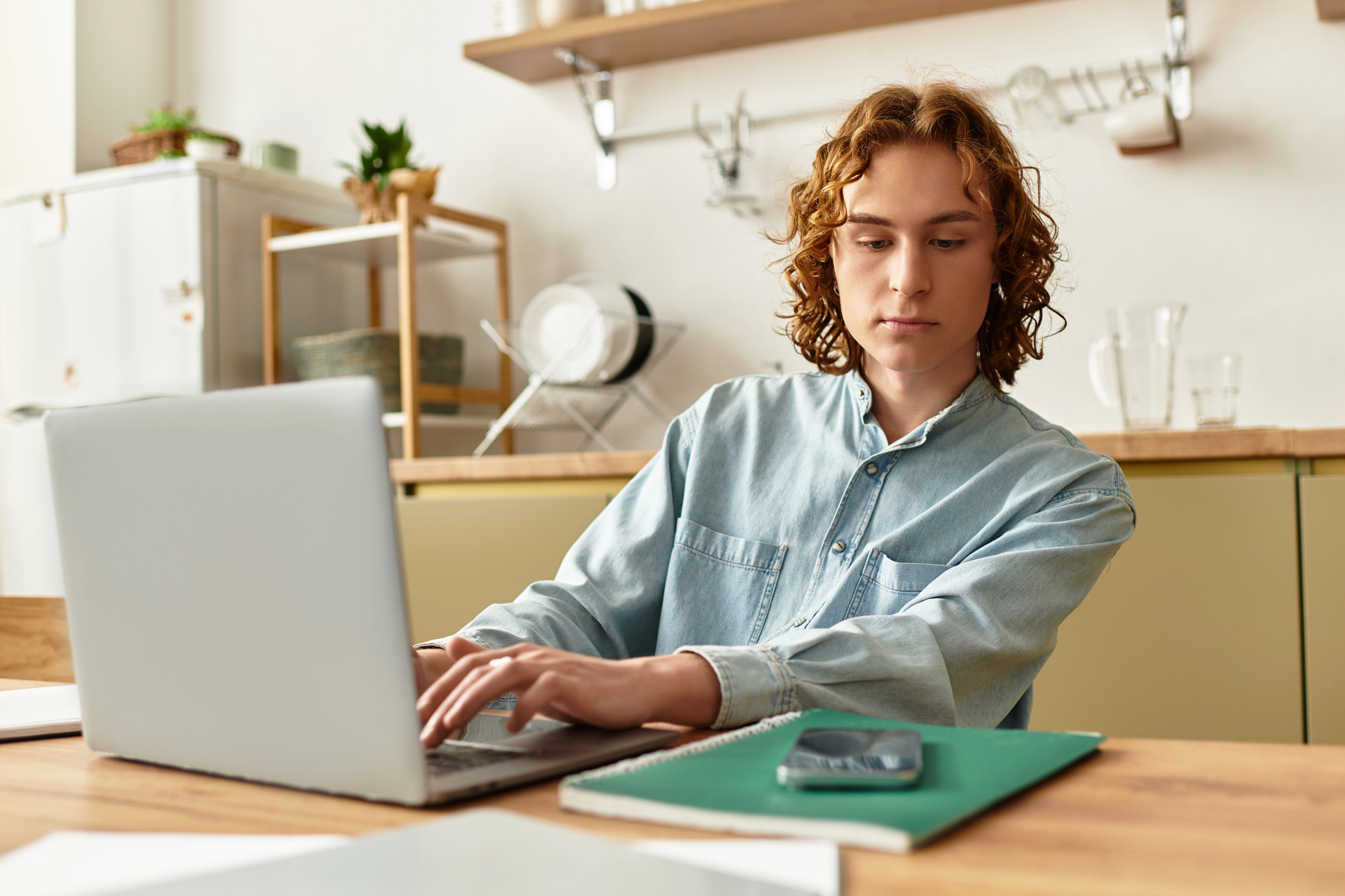 Hombre usando una computadora y mirando un teléfono sobre la mesa