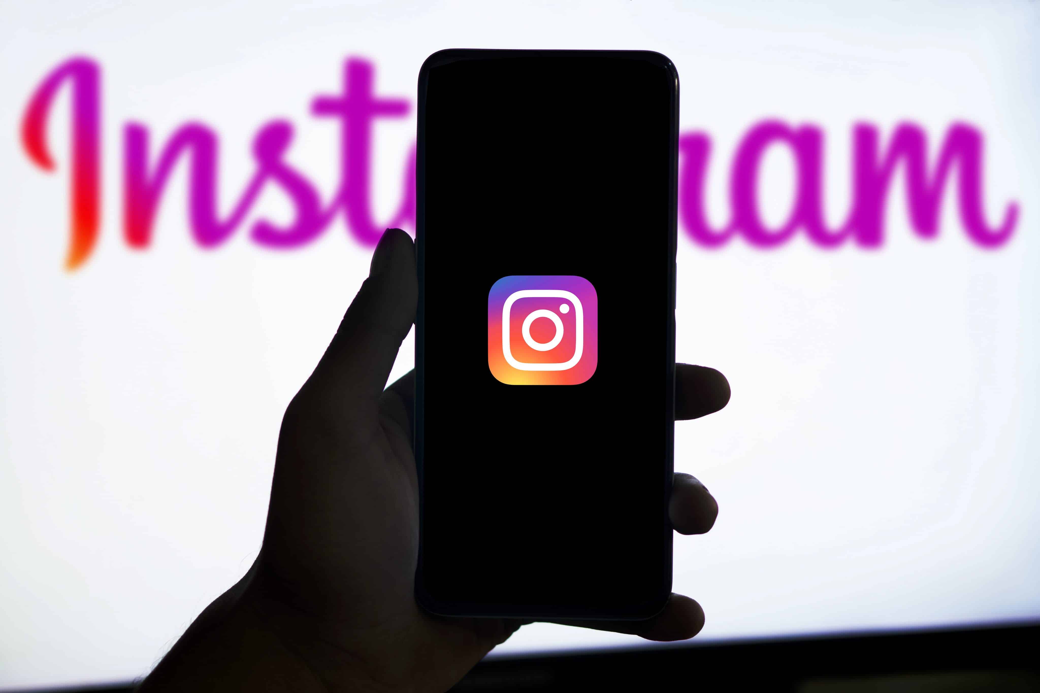 Mano sosteniendo un teléfono con el ícono de Instagram y la marca de la red social en el fondo