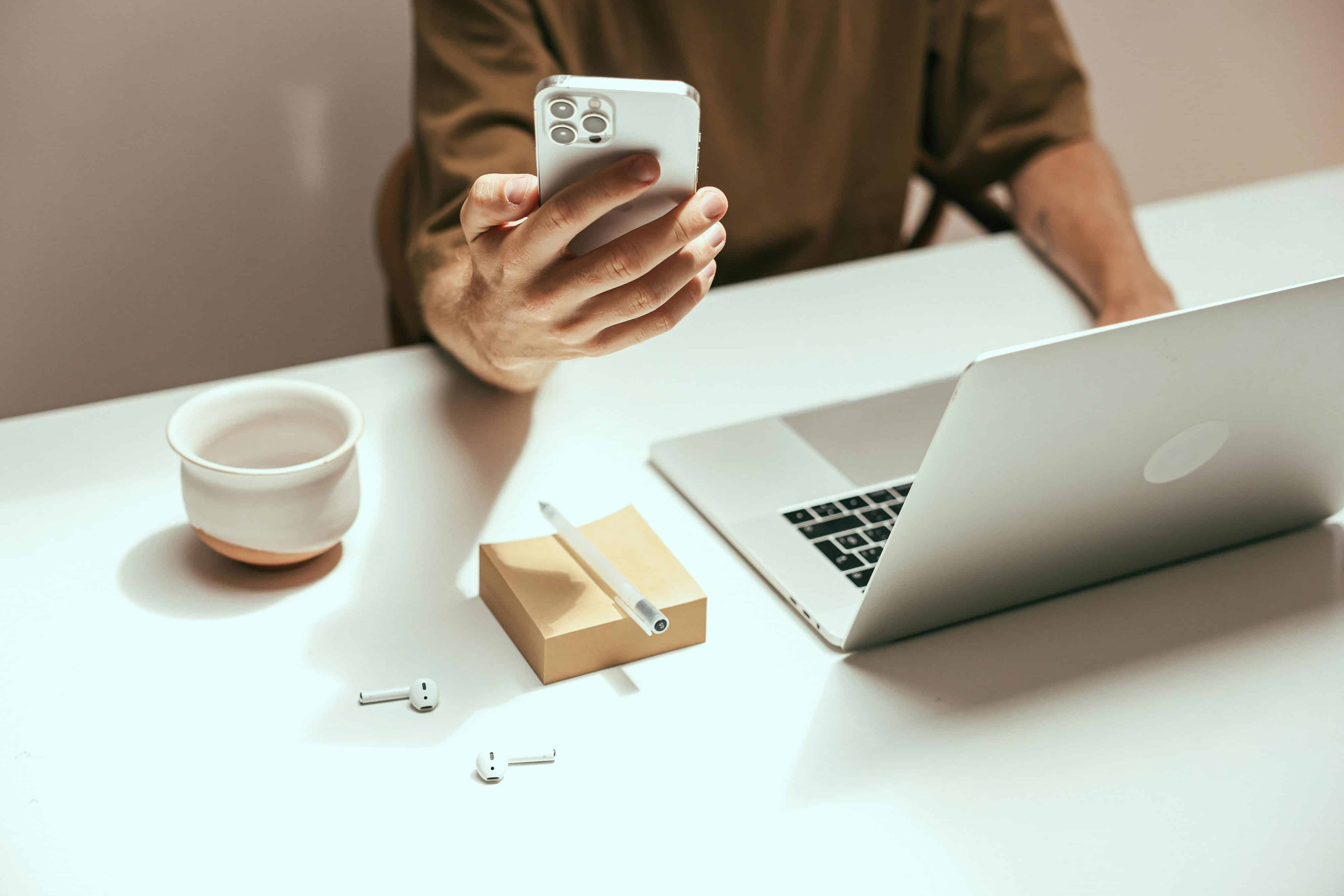 Hombre usando un iPhone con una Mac y AirPods sobre la mesa