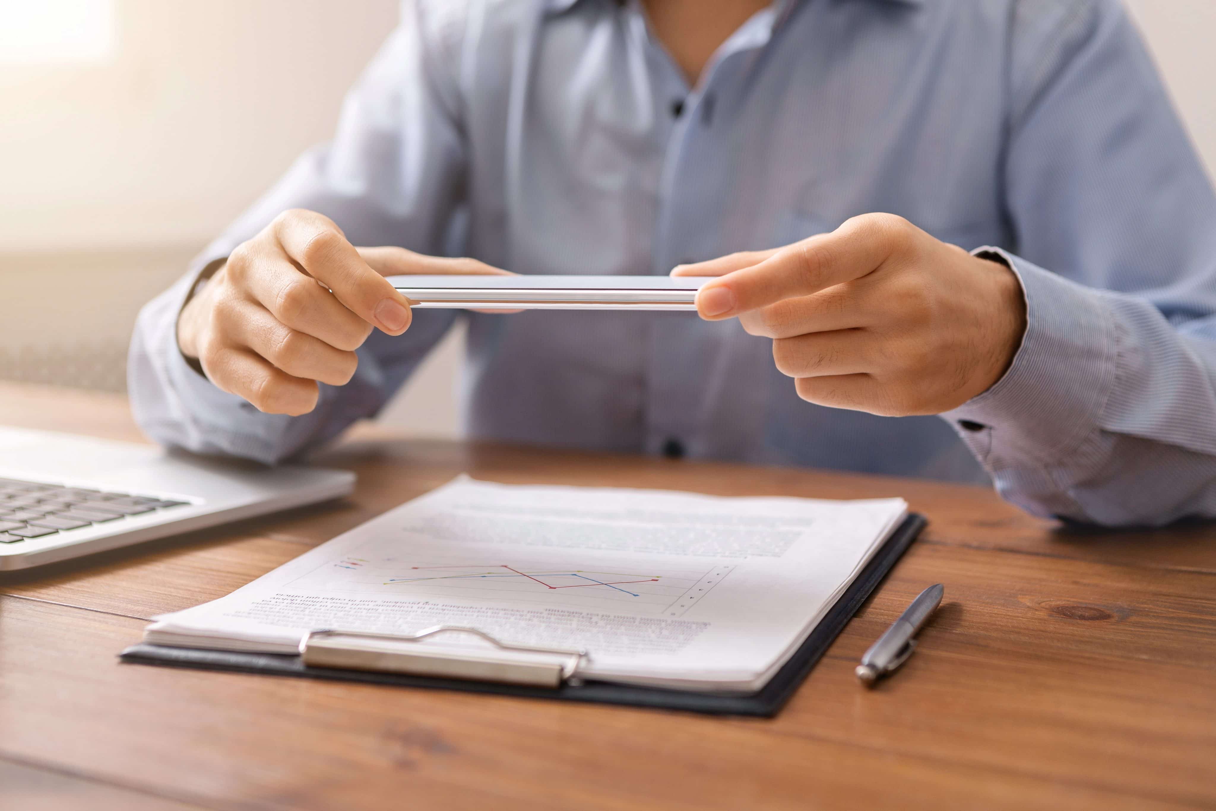 Persona que sostiene un teléfono inteligente horizontalmente tomando fotografías de documentos y usando una aplicación de escáner para hacer copias de documentos