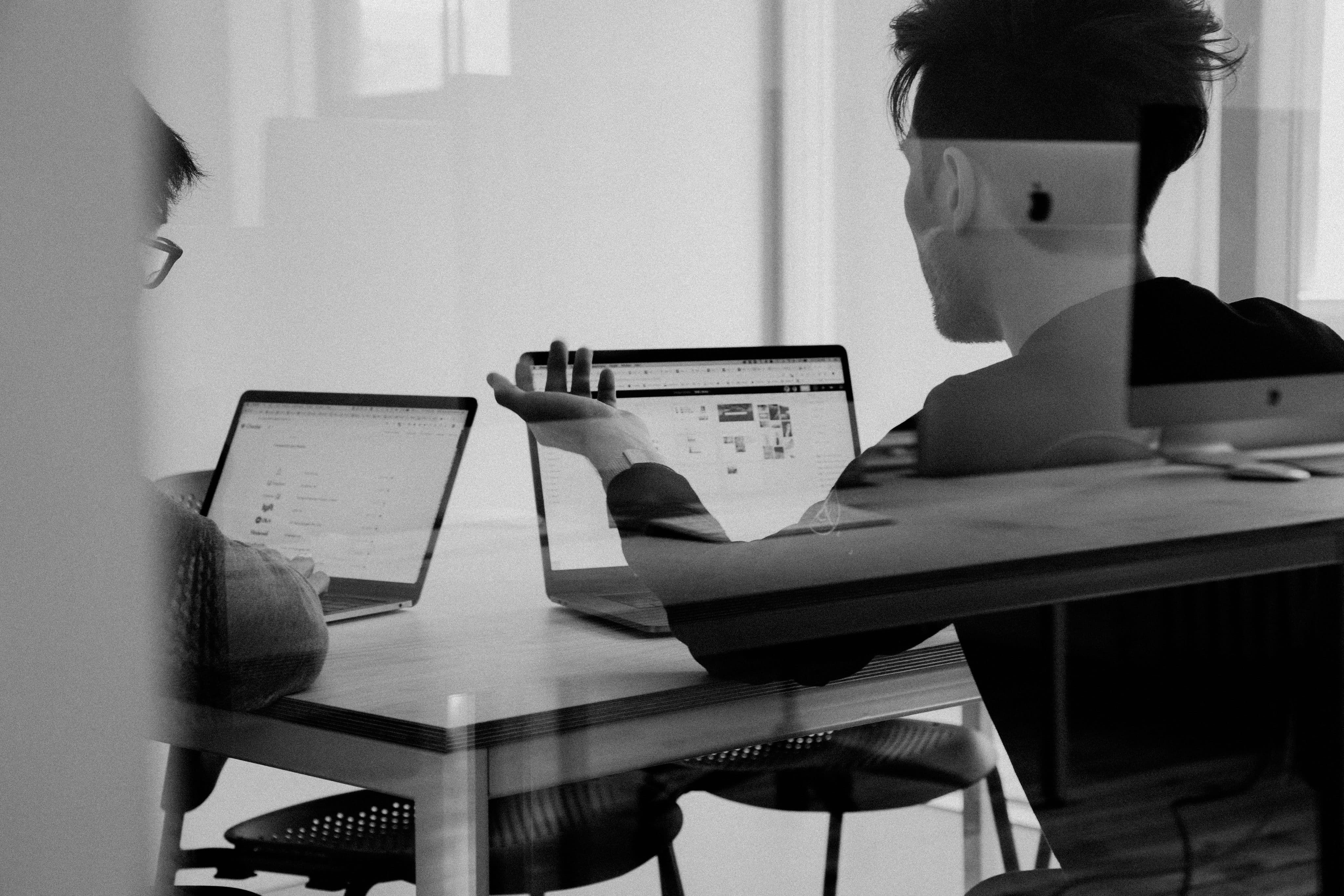 Dos hombres en una habitación hablando y usando Macs